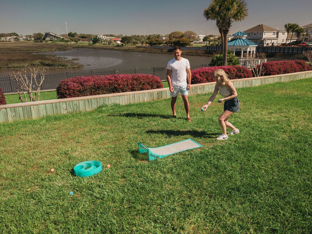 Flyball Classic set laid out on the sand: teal runway ramp, target ring, balls and carry bags by the ocean